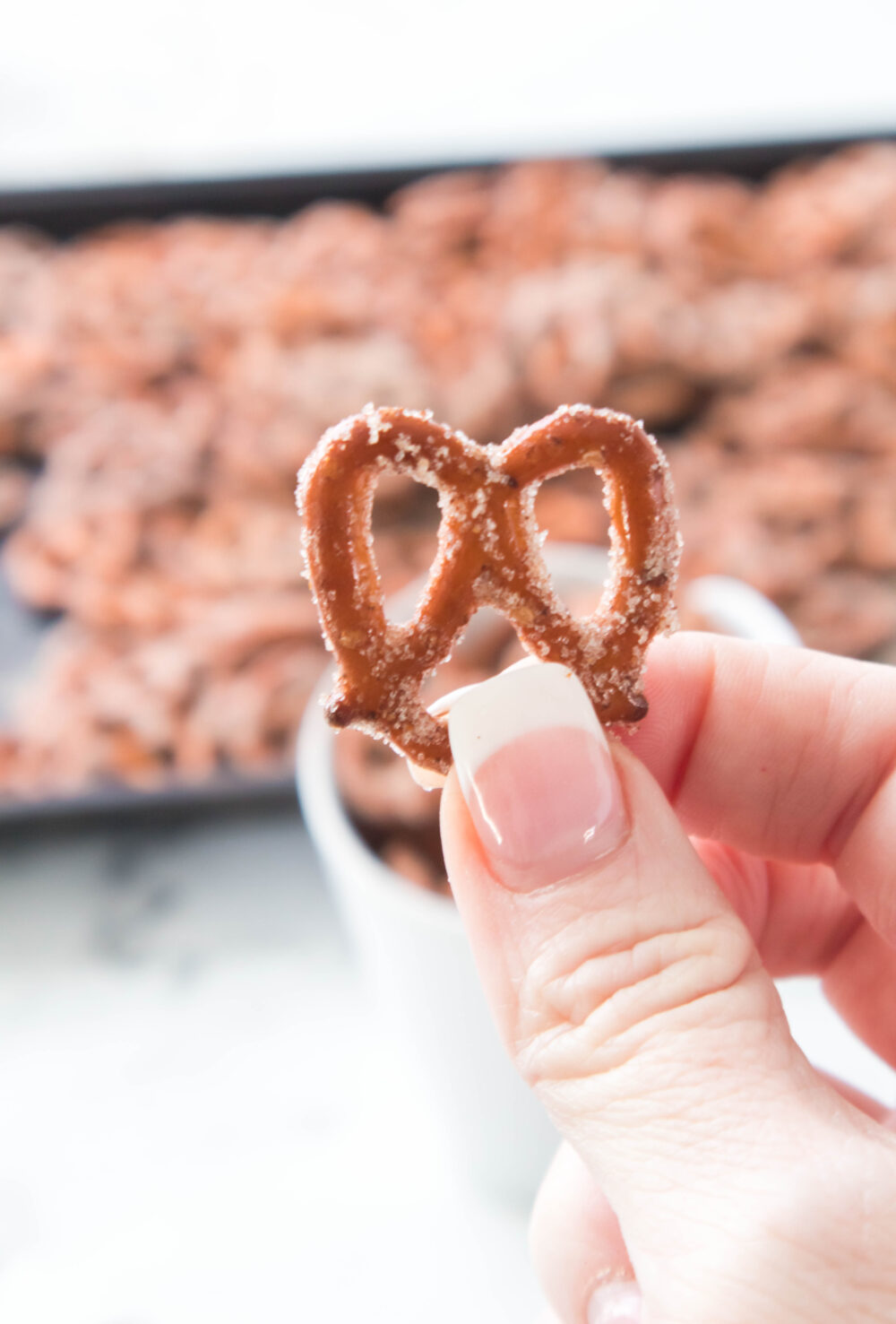 hand holding cinnamon pretzel with baking sheet full of cinnamon pretzels in the background